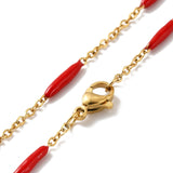 zoomed in sections of golden curb chain and red enamel bar link necklace with lobster claw clasp on white background. 